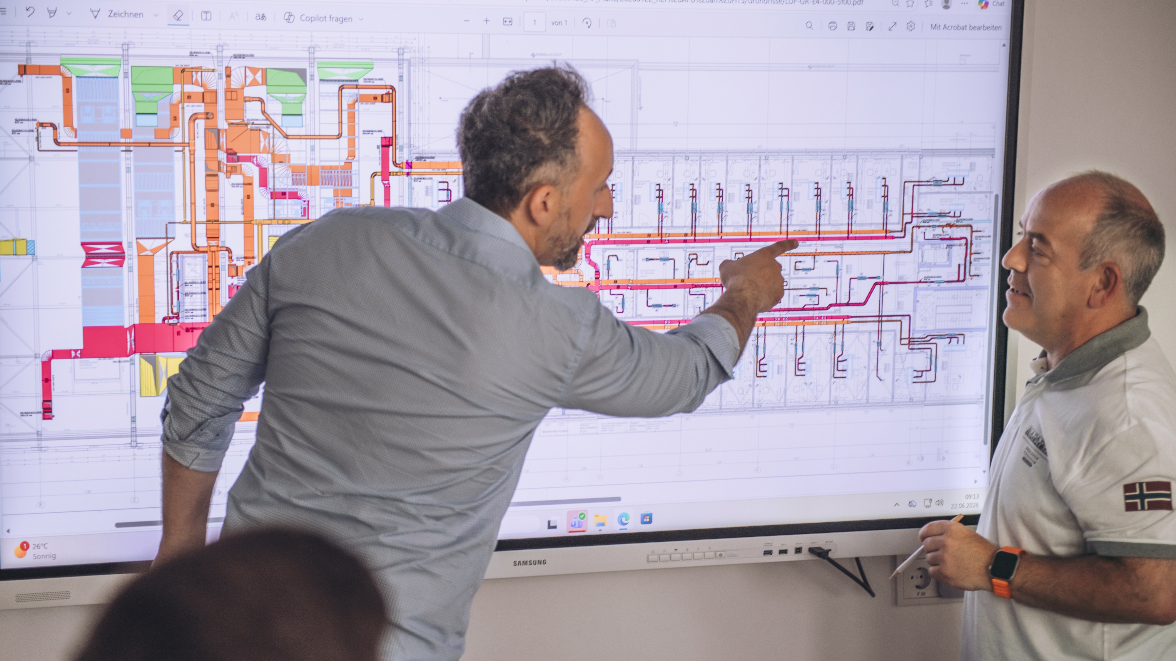 TGA-Planung: ganzheitliche Gebäudetechnik aus einer Hand Mann erläutert einen komplizierten Plan auf einem sehr großen Monitor seinen Kollegen