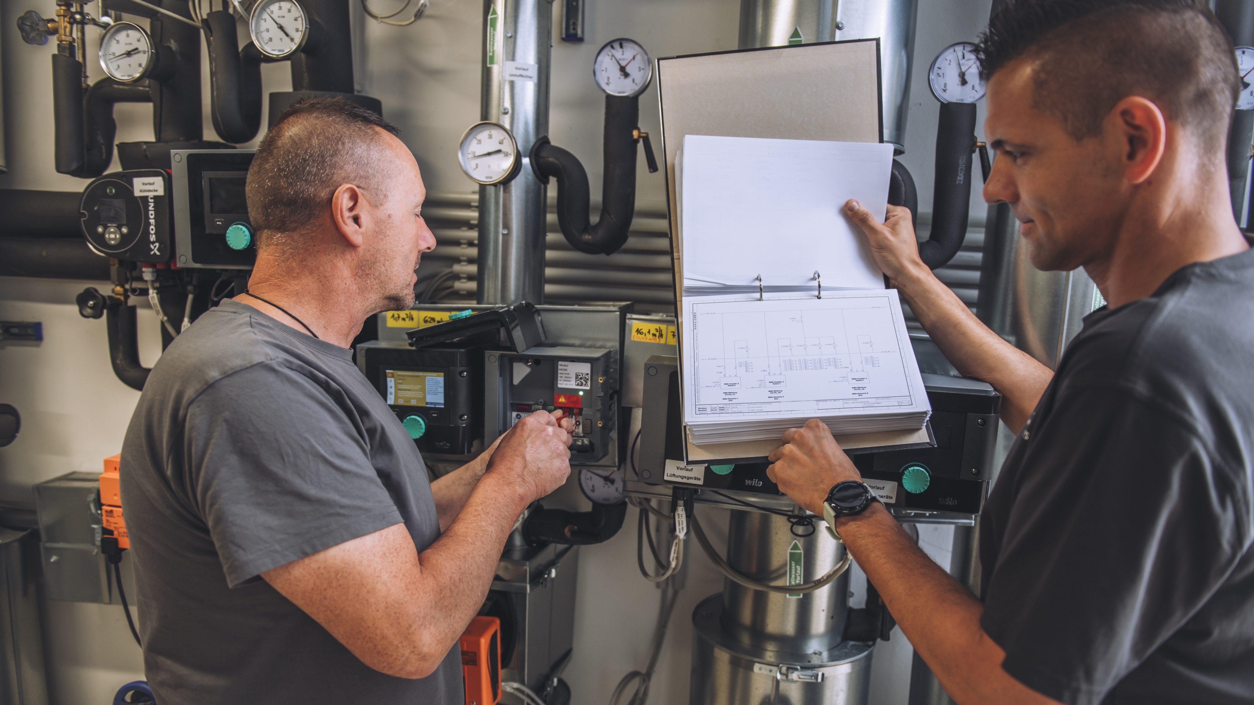 Service & Wartung: damit Ihre Gebäudetechnik zuverlässig läuft Zwei Installateure vor einem technischen Gerät