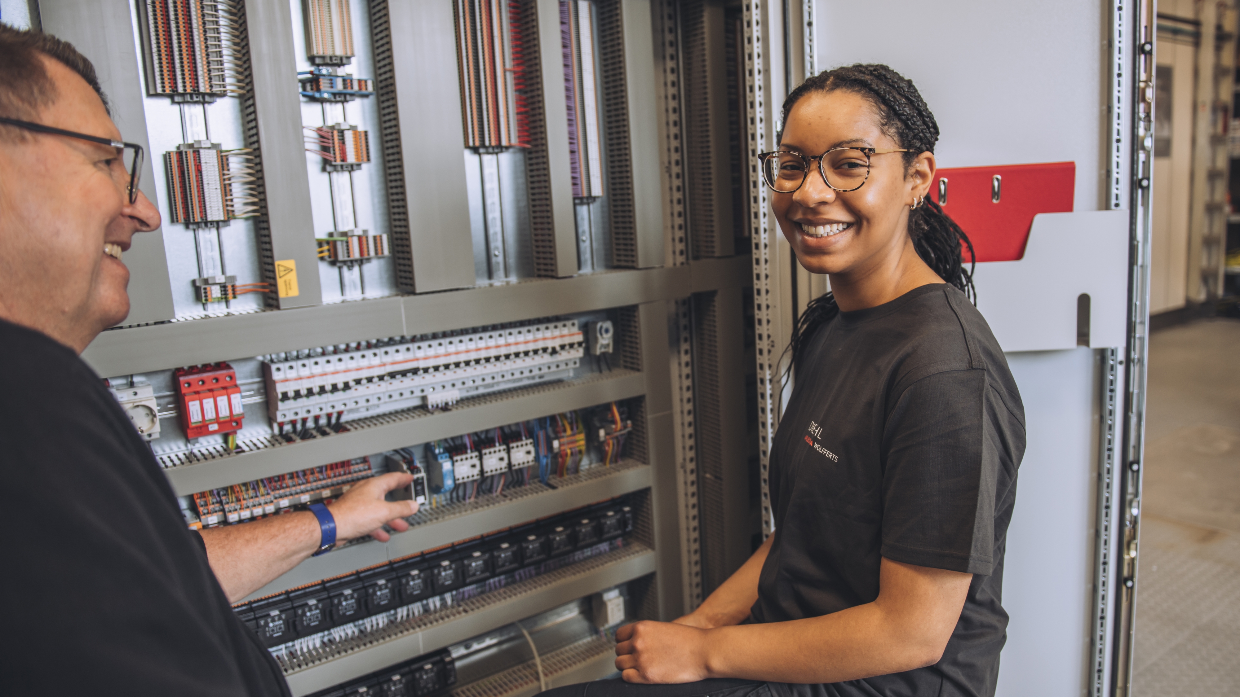 Ausbildung Elektroniker für Energie- und Gebäudetechnik: Deine Ausbildung mit Spannung – im wahrsten Sinne Ausbilder und Auszubildende lachen gemeinsam vor einem geöffneten Schaltschrank